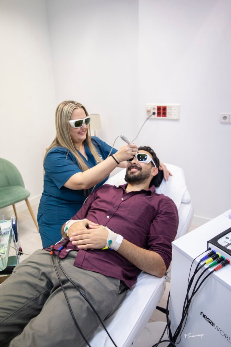Fisioterapeuta aplicando fotobiomodulación láser transcraneal en la frente de un paciente; ambos llevan gafas de protección